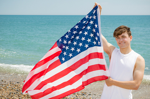 Young adult Caucasian male holding on a beach holding the flag of The United States