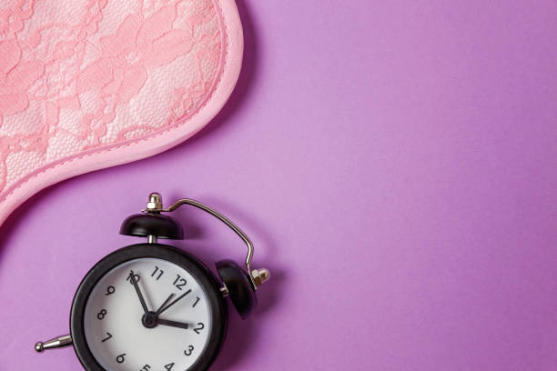 istock Sleeping mask and alarm clock on purple violet background 1152880125