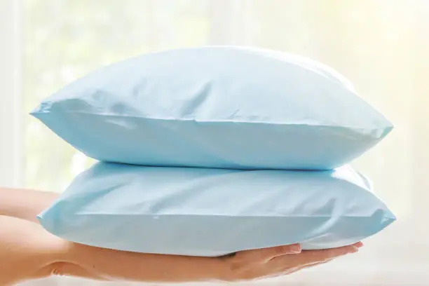 Closeup of hands holding two blue pillows, on blurred background.