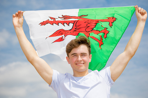 Young adult Caucasian male holding on a beach holding the flag of Wales