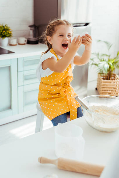 istock excited kid in yellow polka dot apron looking at eggs while cooking dough in kitchen 1152883432