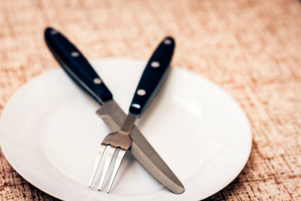 Close-up of a hand placing a stack of white plates with a napkin and cutlery on a wooden table.