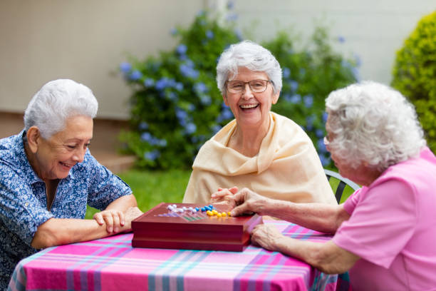 Cheerful elderly women playing boardgame outside Cheerful latin elderly women sitting at a table outside, playing a boardgame and smiling at each other. chinese checkers stock pictures, royalty-free photos & images