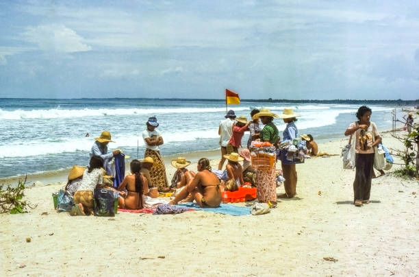 Nostalgic image of Kuta Beach, Balin177. Vendors on the beach sell clouting to tourists sitting in the sand.\n+++Scan of old slides +++