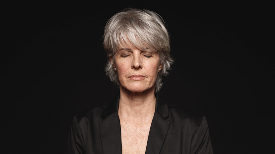 Close up of senior woman with her eyes closed. Woman in formal wear isolated on black background.