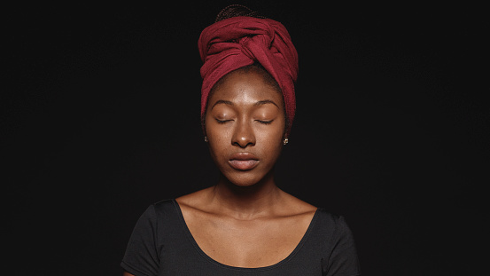 Close up of african woman isolated on black background with eyes closed. African female with a cloth wrapped on head with closed eyes.