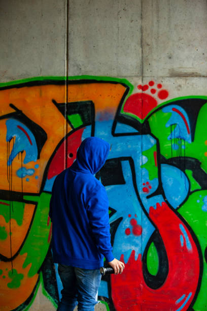istock Graffiti Artist With Hooded Shirt Drawing Graffiti on Wall 1152902875