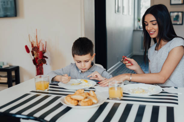 Beautiful young woman at home with her little cute son are having breakfast stock photo