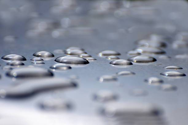 strahlende regentropfen auf einer silbernen oberfläche schließen abstrakt - beaded water stock-fotos und bilder