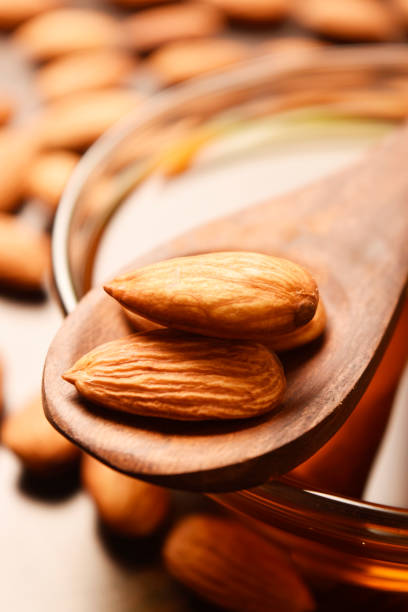 almonds in wooden spoon with oil bowl, vertical image, wallpaper stock photo