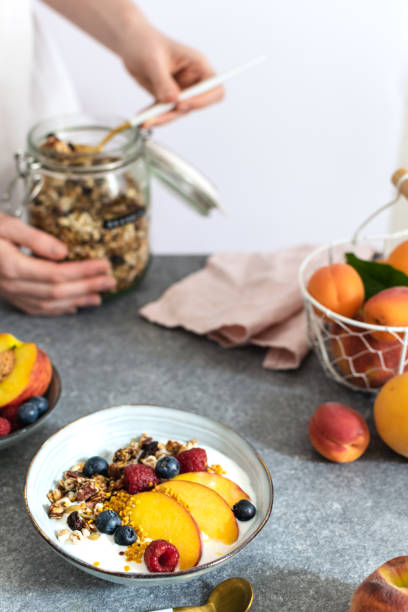 istock Female hands serving granola from jar, with greek yogurt fresh peach, blueberry, raspberry on the table - healthy breakfast 1152913281