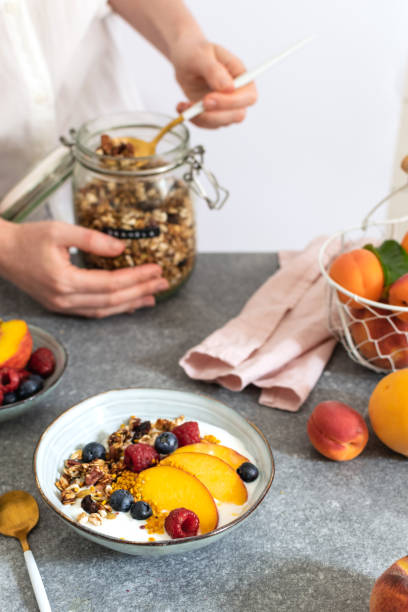 istock Female hands serving granola from jar, with greek yogurt fresh peach, blueberry, raspberry on the table - healthy breakfast 1152913293