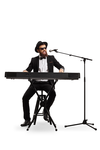 Full length portrait of a male musician playing a digital piano and singing on a microphone isolated on white background