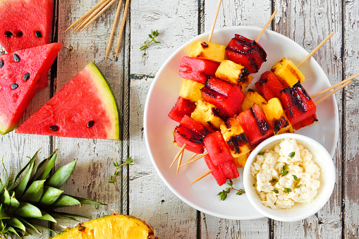 Grilled watermelon and pineapple fruit kabobs with feta. Top view on a white wood background. Summer food concept.