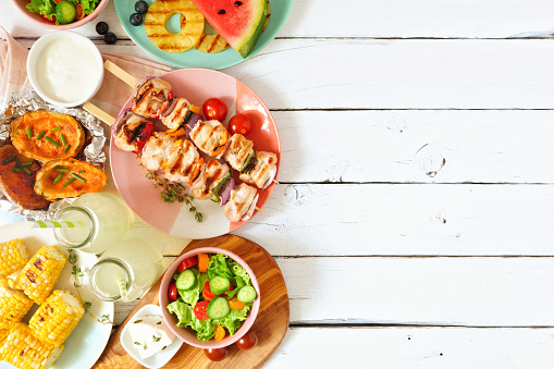 Summer BBQ or picnic food side border. Selection of grilled meat, fruits, salad and potatoes. Above view over a white wood background. Copy space.