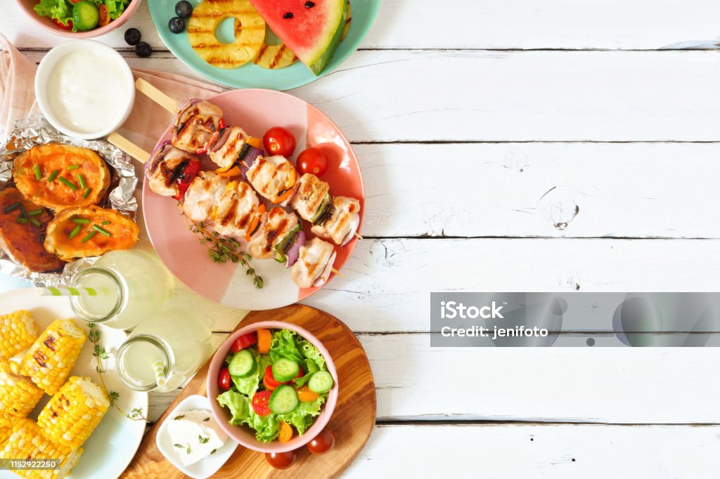 Summer BBQ or picnic food side border, above view over a white wood background Summer BBQ or picnic food side border. Selection of grilled meat, fruits, salad and potatoes. Above view over a white wood background. Copy space. Food Stock Photo
