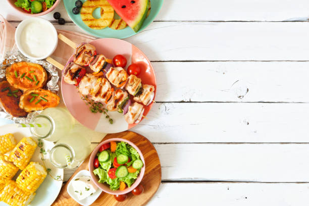 Summer BBQ or picnic food side border, above view over a white wood background Summer BBQ or picnic food side border. Selection of grilled meat, fruits, salad and potatoes. Above view over a white wood background. Copy space. barbecue grill food stock pictures, royalty-free photos & images