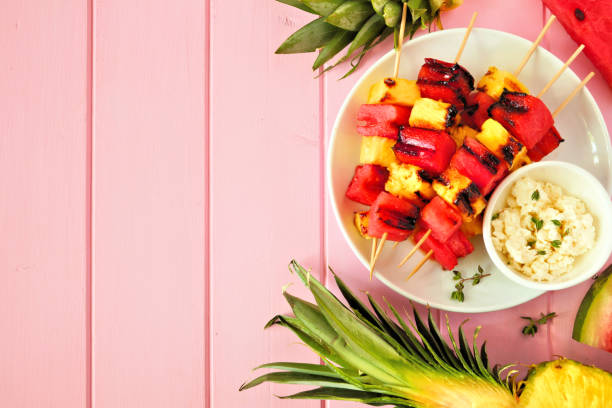 istock Grilled summer watermelon and pineapple fruit kabobs, top view side border on a pink wood background 1152922494