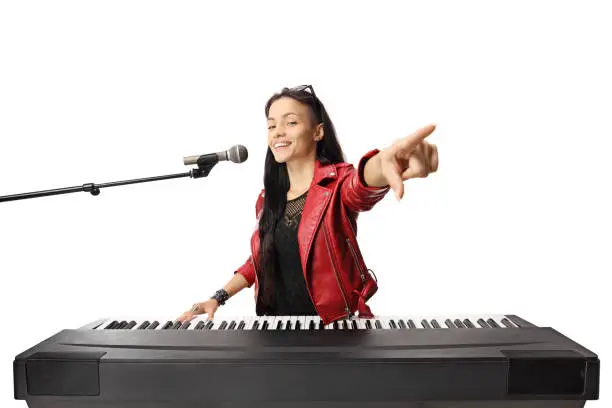Photo of Young female musician playing a digital piano, singing on a microphone and pointing