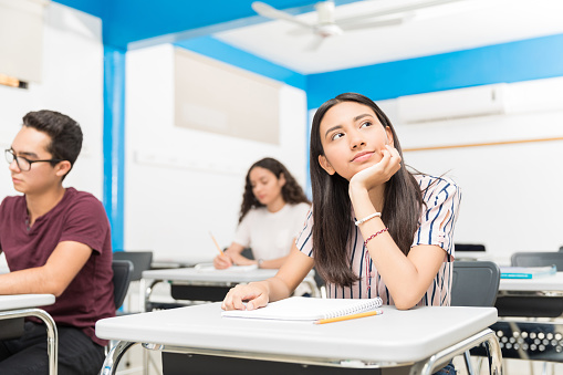 Thoughtful teen sitting with classmates during lecture at high school