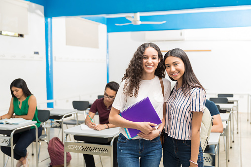 Latin smiling friends standing in classroom at high school