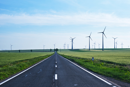Road going forward with wind turbines on its sides and into the distance, on blue skies. Concept for new, better, non polluting, sustainable energy solutions.