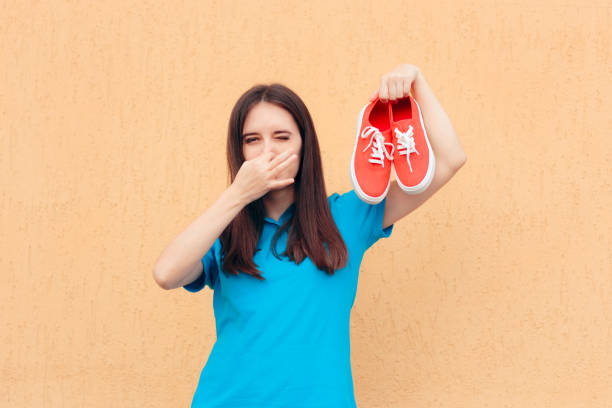 Woman Covering Nose Holding a Pair of Stinky Shoes Smelly gumshoes in need for odor remover unpleasant smell stock pictures, royalty-free photos & images