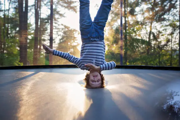 Sweet preteen boy jumping on trampoline making somersaults in the air. Child levitating. Happy child jumping on sunset