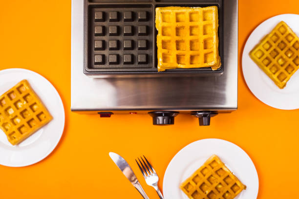 Mother and son making waffles in the morning. They are both wearing casual summer clothes and colourful aprons. Interior of kitchen in private home.