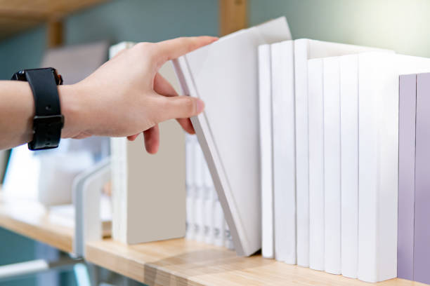 Male hand picking white book on bookshelf Male hand choosing and picking white book on wooden bookshelf in public library. Education research and self learning in university life concepts opportunity dictionary definition stock pictures, royalty-free photos & images