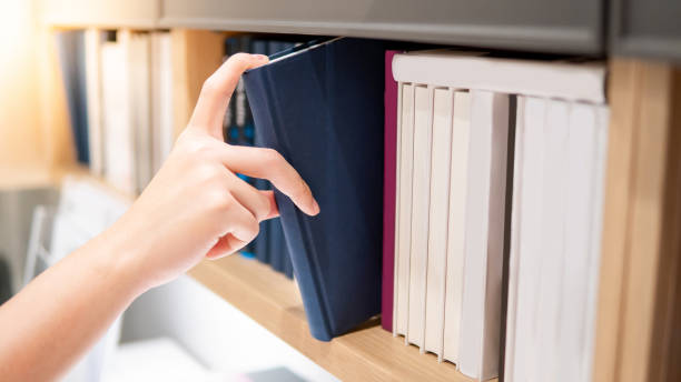 istock Male hand picking blue book on bookshelf 1152990536