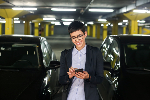 Young businesswoman in a parking garage, using a mobile app. About 20 years old, Caucasian female.