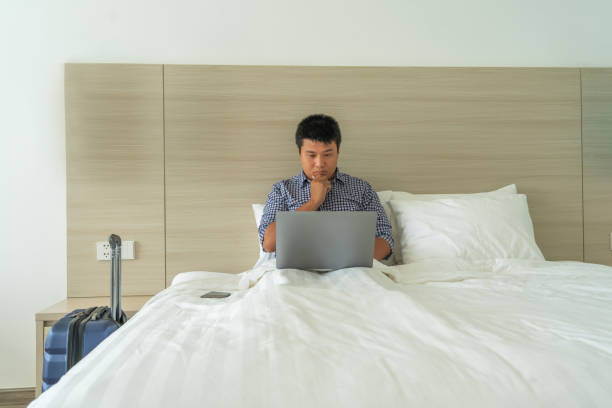 istock Businessman using laptop on bed next to suitcase in hotel 1152994993