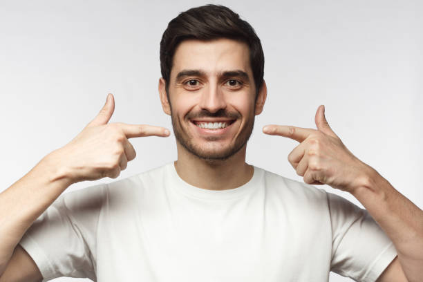 porträt des lächelnden jungen mannes, der nach der aufhellung auf seine perfekten natürlichen weißen zähne zeigt. zahnklinik anzeigen konzept - teeth model stock-fotos und bilder