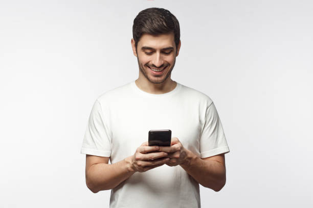 istock Young man standing, looking at screen of cellphone with smile, browsing web pages or chatting with friend, isolated on gray background 1153003756