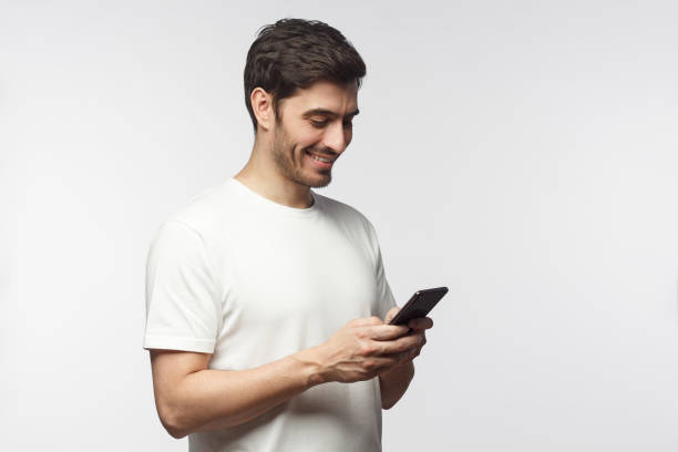 istock Side portrait of handsome man, isolated on gray background, looking down at smartphone screen, exchanging messages or surfing internet 1153003776