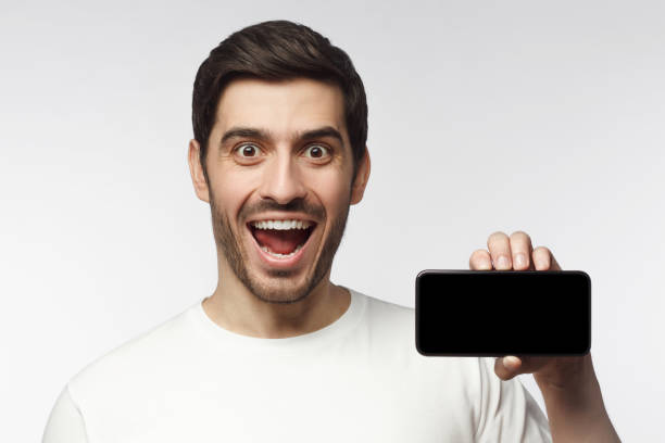 istock Young excited man showing blank screen smartphone in hand, isolated on gray background 1153003777
