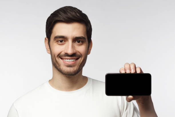 istock Young smiling man showing blank screen smartphone in hand, isolated on gray background 1153003783