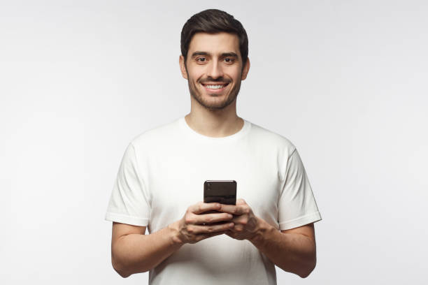 istock Handsome smiling man looking at camera while holding his smart phone, isolated on gray background 1153003798