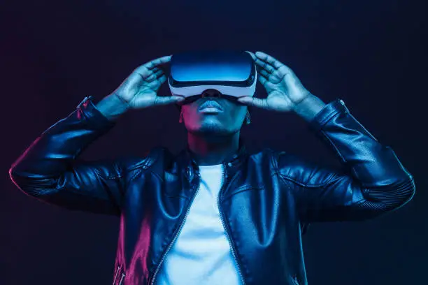 Photo of African american man in vr glasses, watching 360 degree video with virtual reality headset isolated on black background
