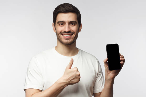 istock Handsome smiling young man holding blank smartphone, showing thubms up gesture, isolated on gray background 1153003882