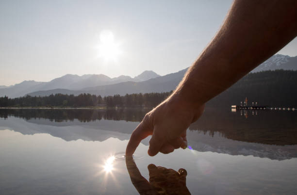 les mains de l’homme descendent pour toucher la surface de l’eau au lever du soleil - water touching sensory perception using senses photos et images de collection