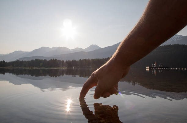 les mains de l’homme descendent pour toucher la surface de l’eau au lever du soleil - water touching sensory perception using senses photos et images de collection