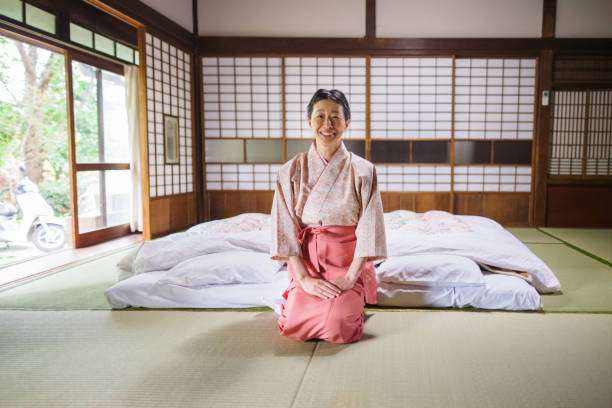 Portrait of Japanese inn owner sitting in room A portrait of a female Japanese inn owner sitting on tatami in a room and looking at camera. traditional japanese bed stock pictures, royalty-free photos & images
