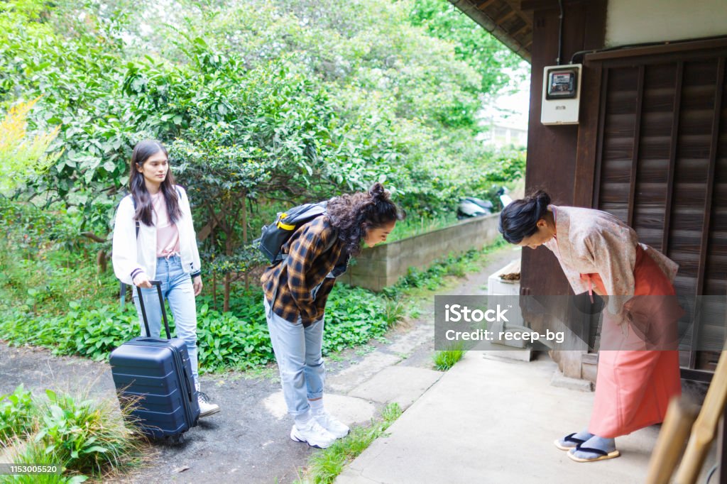 Owner of Japanese inn greeting female tourists from oversees An owner of a Japanese inn is greeting her female tourists from oversees at the entrance. Bowing Stock Photo