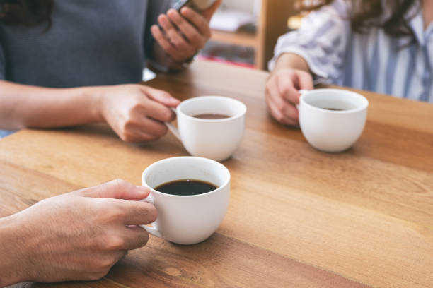 istock Closeup image of people using mobile phone and drinking coffee together 1153011372