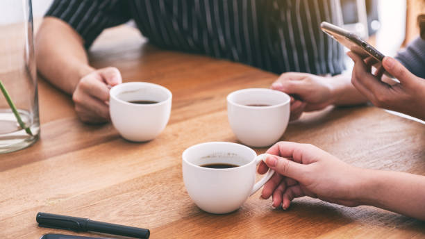 istock Closeup image of people using mobile phone and drinking coffee together 1153011389