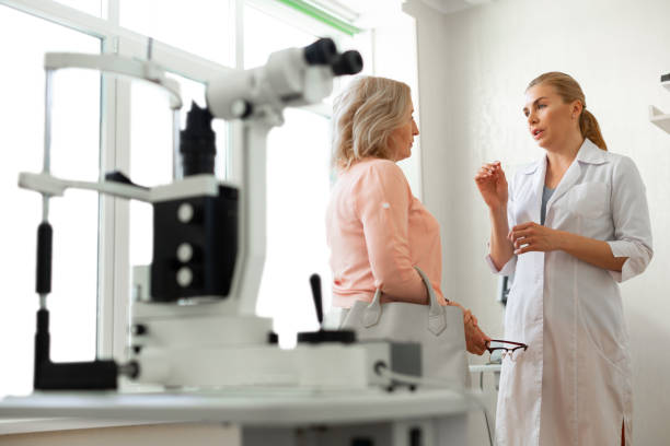 Diligent long-haired ophthalmologist actively gesturing while talking Filled with technique. Diligent long-haired ophthalmologist actively gesturing while talking with calm short-haired woman eye care professional stock pictures, royalty-free photos & images