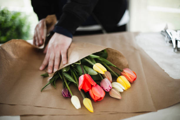 haufen regenbogen-tulips in braunem papierwickel - blumenhändler stock-fotos und bilder