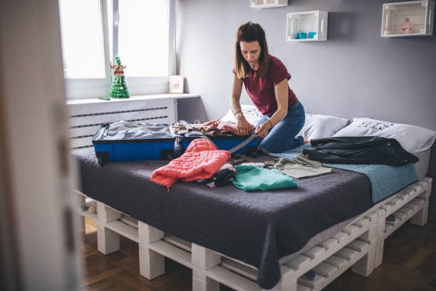 istock Young woman sitting on bed and packing suitcase 1153039590